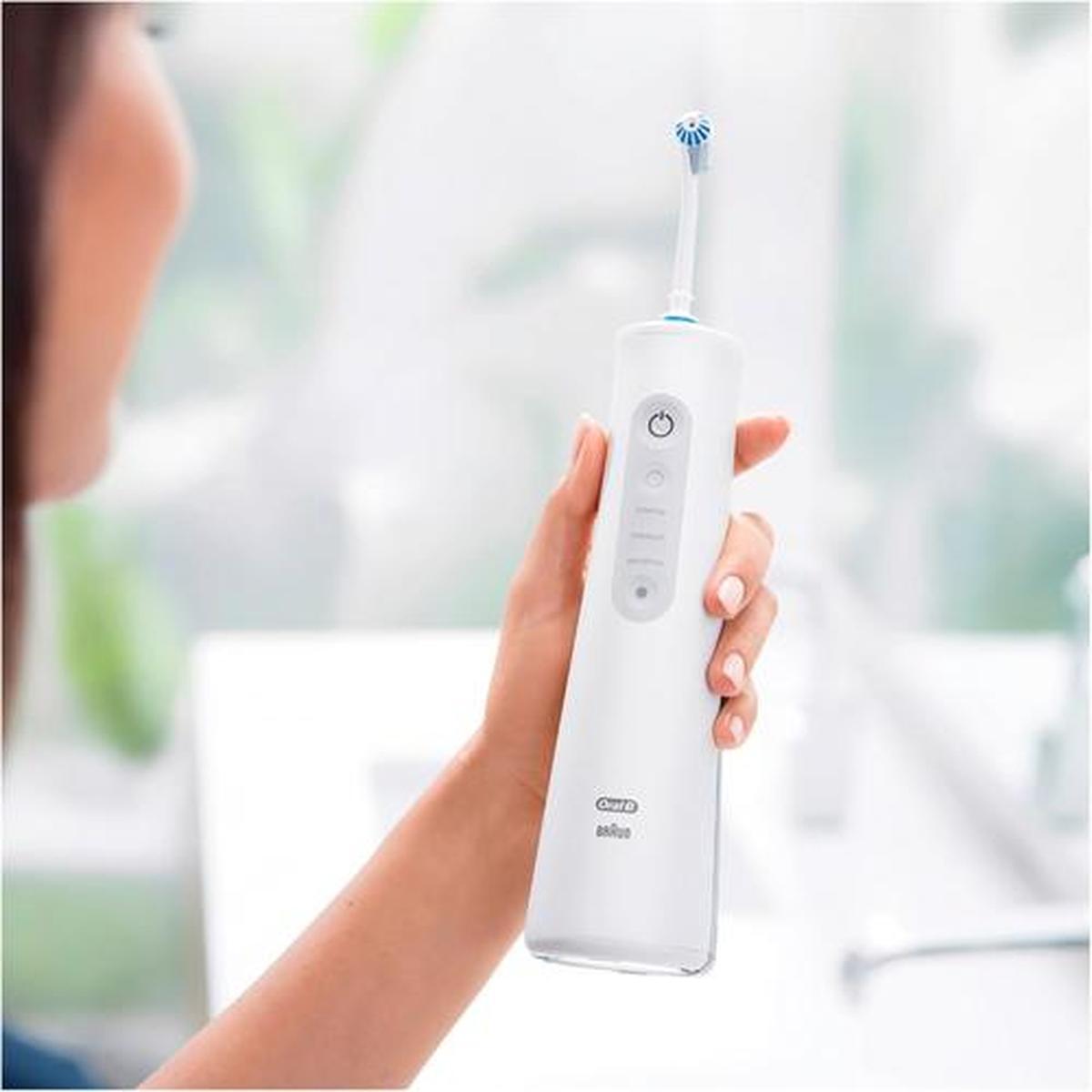 White Oral-B Aquacare cordless dental irrigator held in a hand, featuring adjustable intensity settings and a slim design.