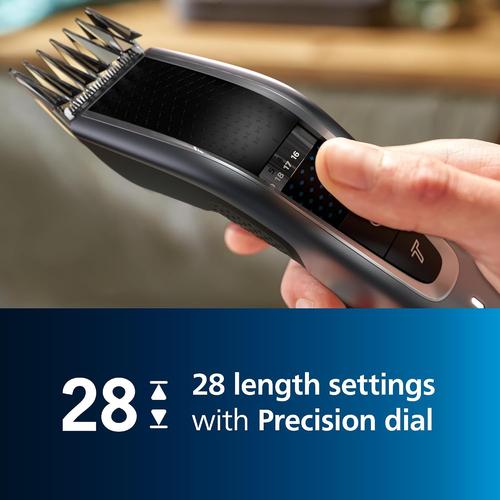 Hand holding a black Philips Series 5000 hair clipper with a precision dial for 28 adjustable length settings.