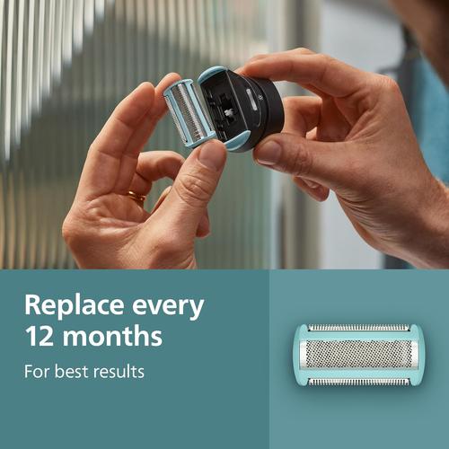 Hands holding a light blue Philips body groomer replacement foil head with a metallic shaver screen and protective trim guards.