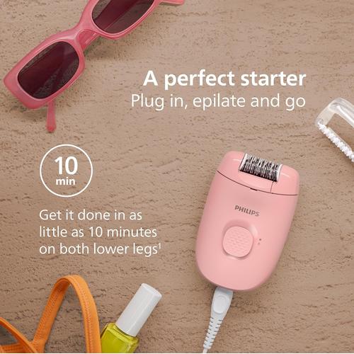 Compact pink Philips corded epilator with massage cap, displayed on a textured surface with sunglasses and nail polish.