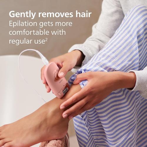 Compact pink Philips corded epilator being used on a leg, featuring a massage cap and ergonomic non-slip grip design.
